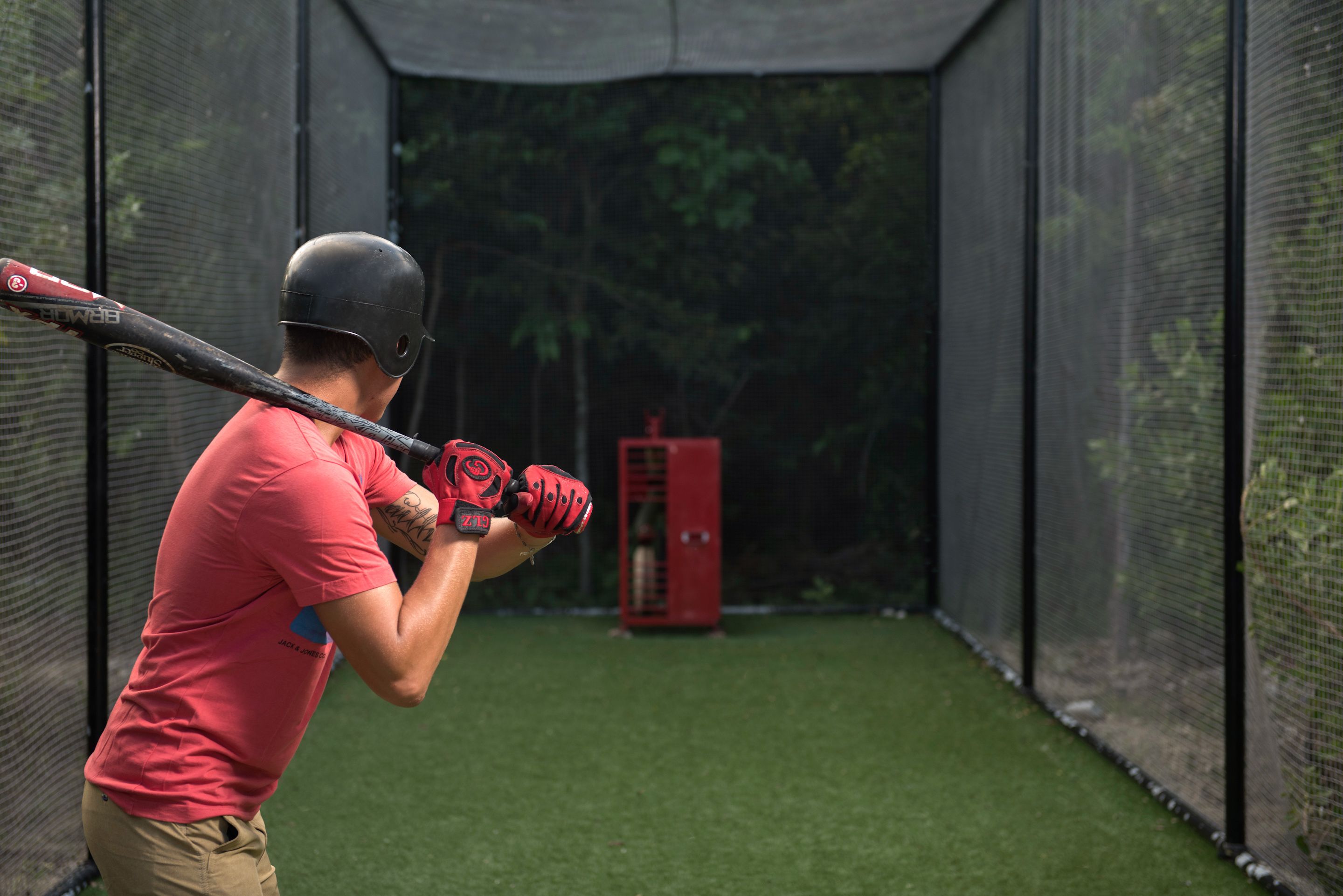 A batting cage with a netted enclosure, artificial turf, and a red batting tee.