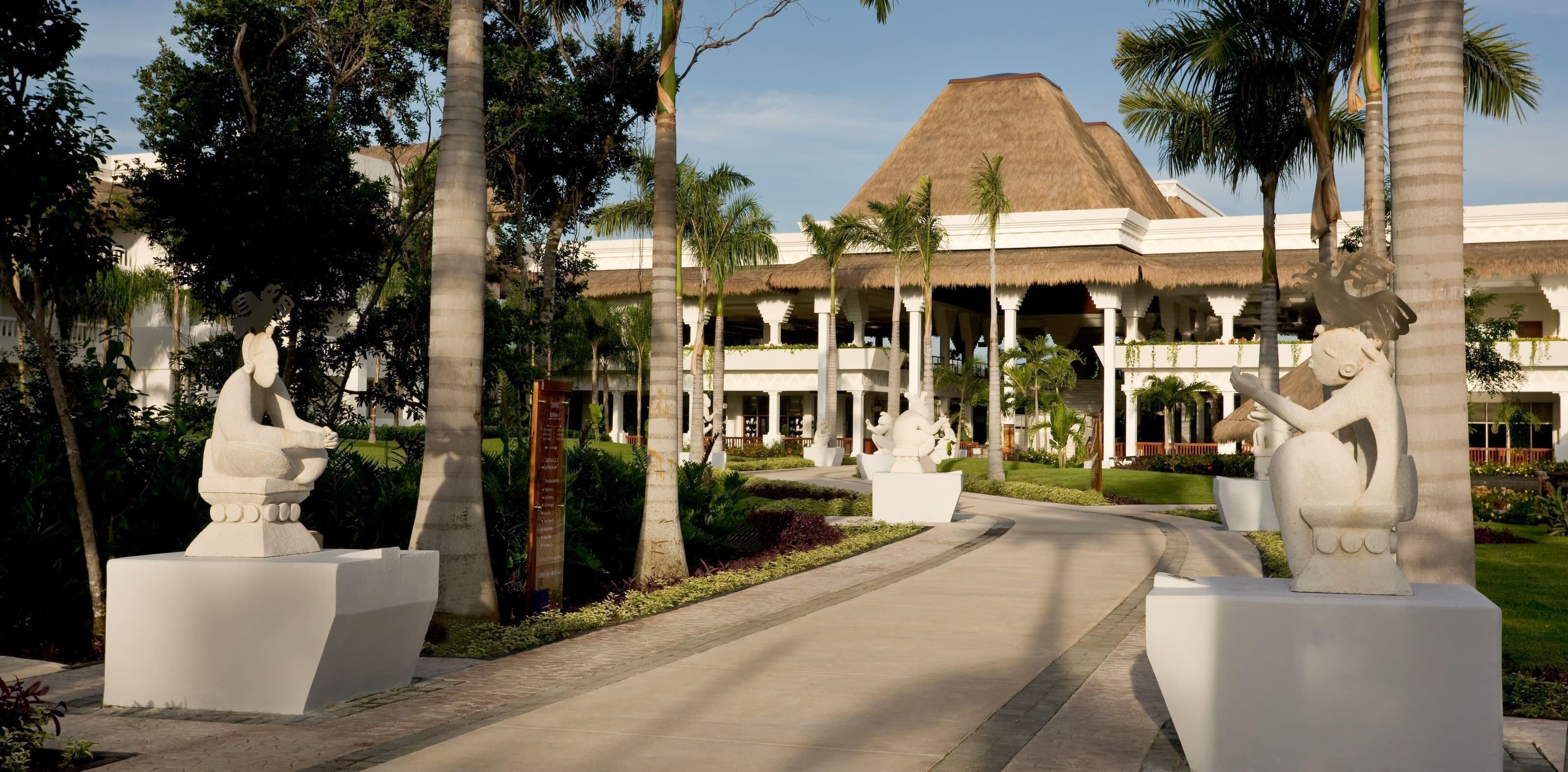 A resort with a thatched-roof building, palm trees, and stone statues.