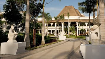 Un resort con un edificio de techo de paja, palmeras y estatuas de piedra.