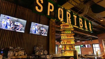 Un bar con un letrero que dice "SPORTBAR", múltiples pantallas mostrando deportes, y una variedad de botellas y vasos en estantes.