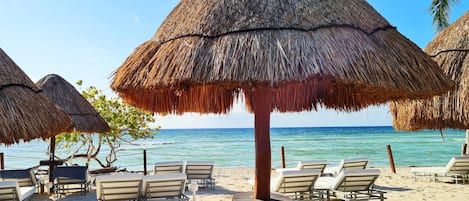 Una playa con sombrillas de paja y sillas de descanso.
