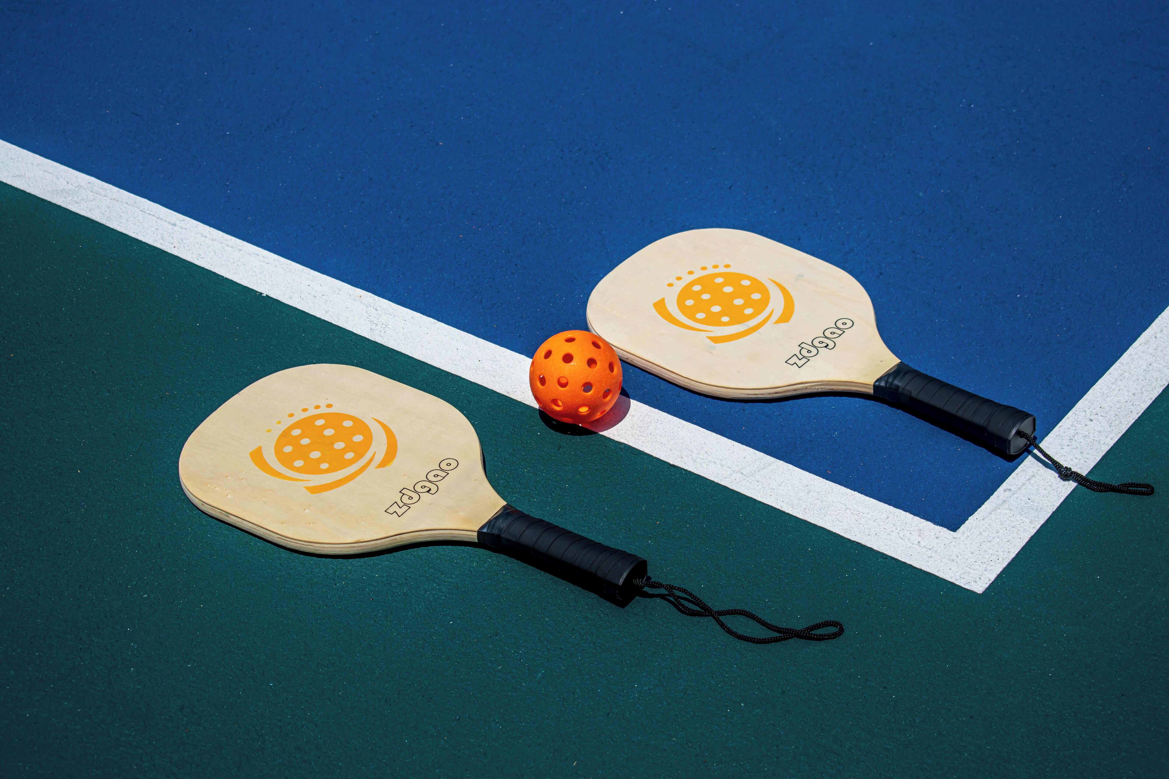 Two paddleball paddles and a ball on a blue and green court.