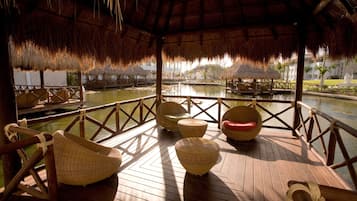 A wooden deck with wicker furniture, a thatched roof, and a view of a water body.