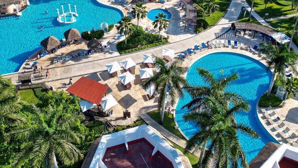 Un resort con varias piscinas, palmeras y vista al océano.