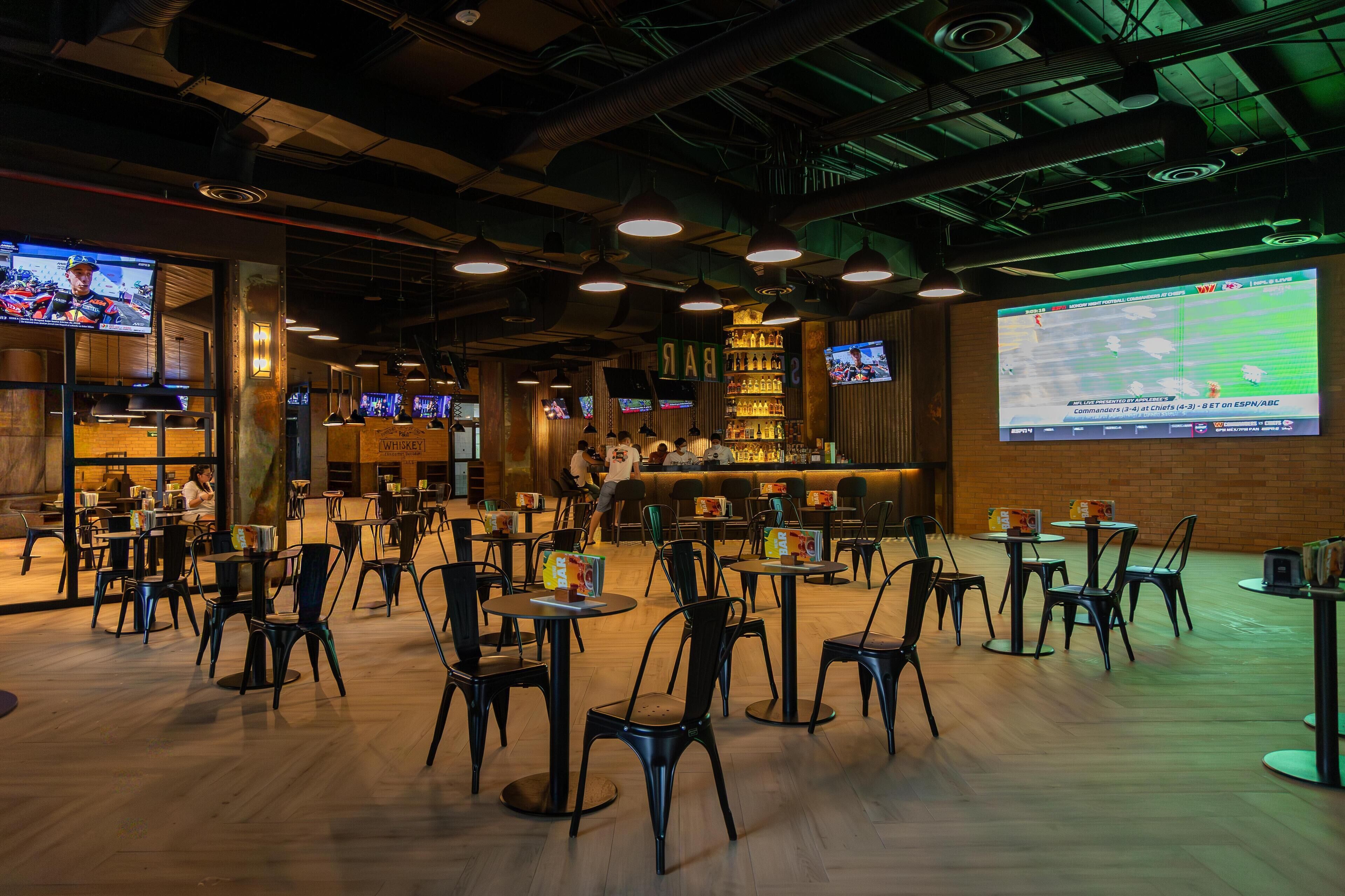 A bar area with multiple TVs displaying sports, a bar counter, and several tables and chairs.