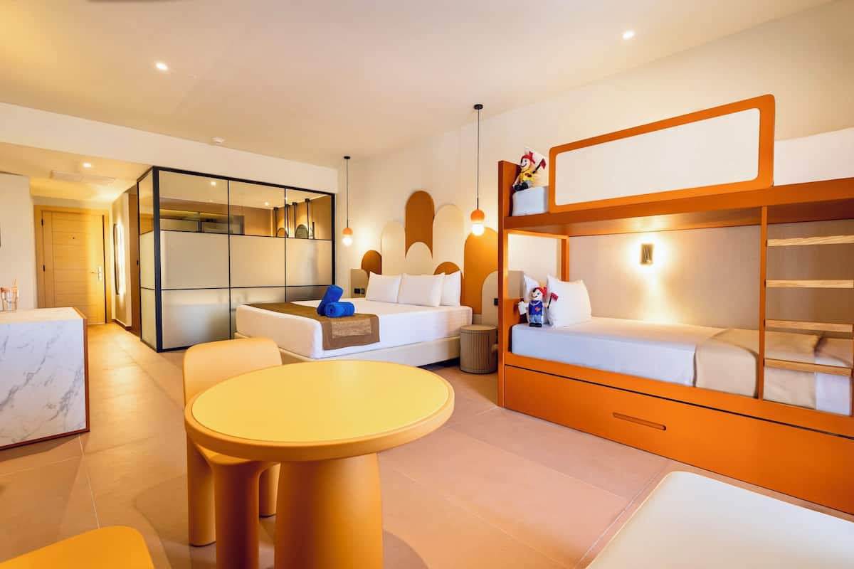 A modern hotel room with a sofa, a small round table, a bunk bed, and a large mirror.