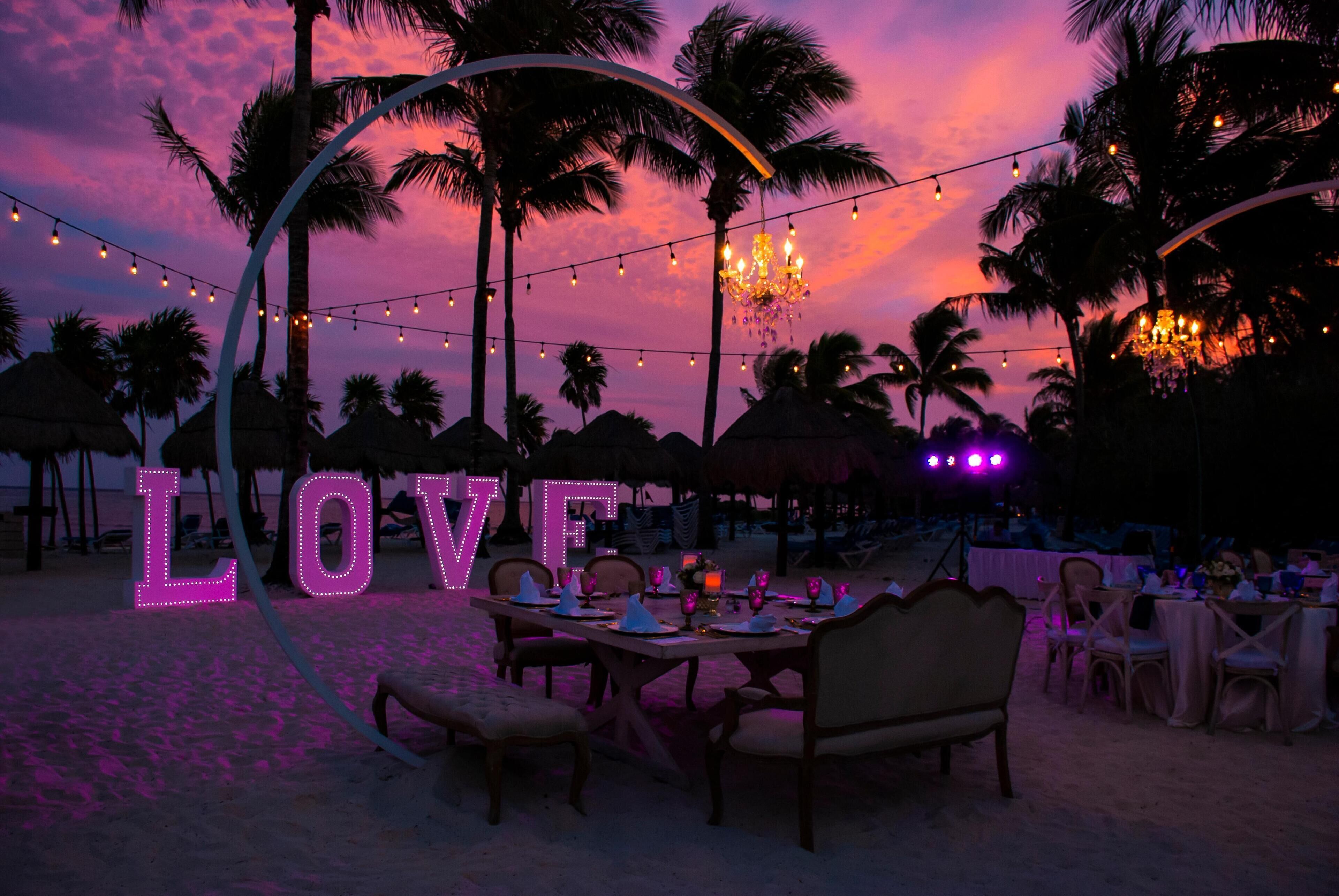 An outdoor dining area with a 'LOVE' sign, string lights, and palm trees.