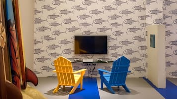 Ein Zimmer mit Fischmuster-Tapete, einem an der Wand befestigten Flachbildfernseher und zwei bunten Adirondack-Stühlen.