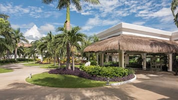 Der Eingang eines Resorts mit einem Reetdach, Palmen und einem gepflegten Garten.