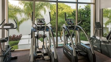 Une salle de sport équipée de tapis de course et d’appareils d’exercice, dotée de grandes fenêtres et offrant une vue sur la verdure.