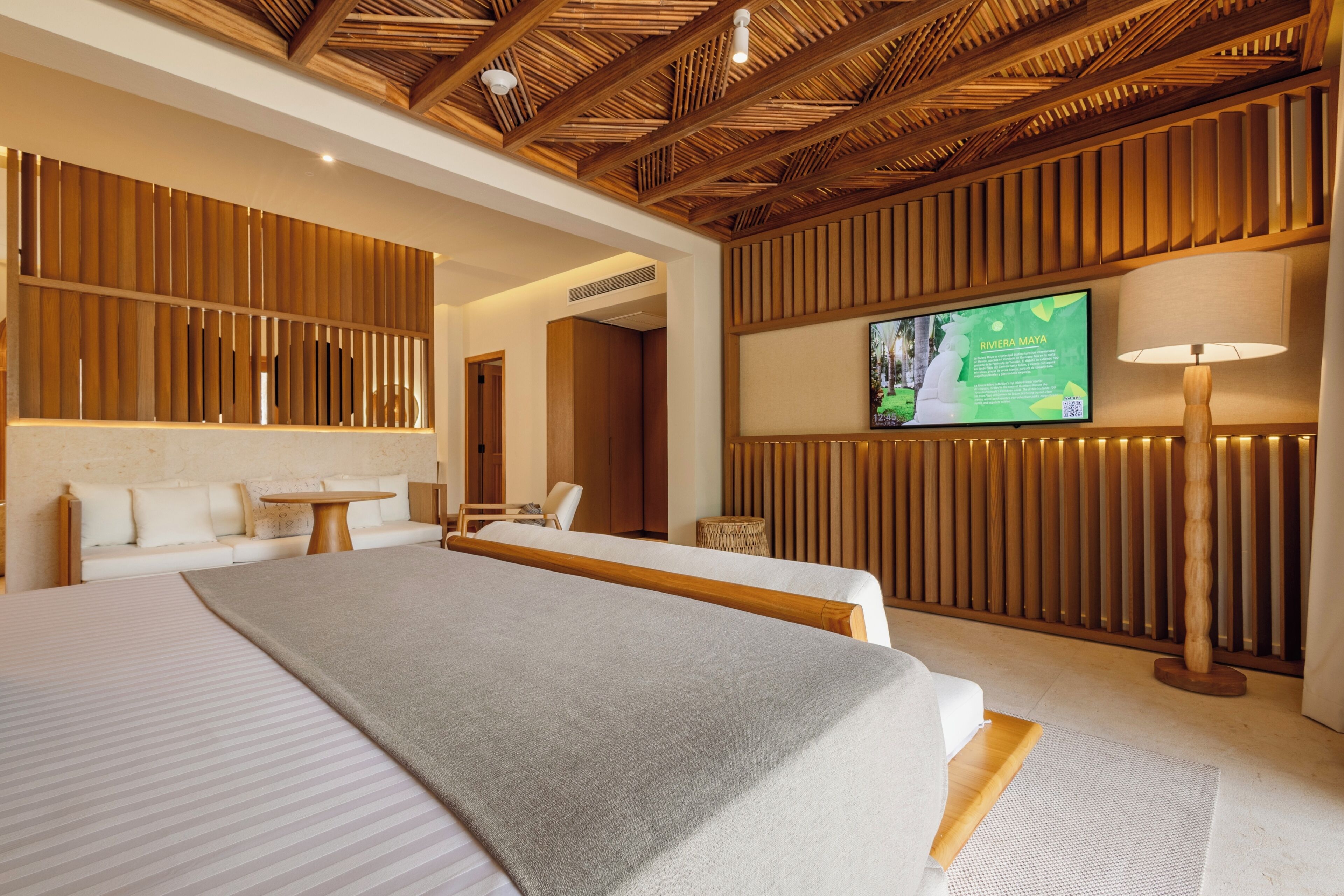 A hotel room with a large bed, a television mounted on the wall, and a wooden ceiling.