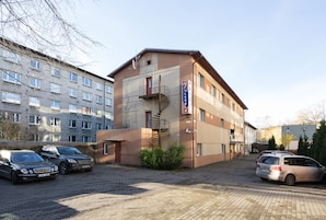 Een hotel met een bakstenen gevel, een zichtbare trap naar de bovenverdieping en een parkeerplaats met meerdere auto's.