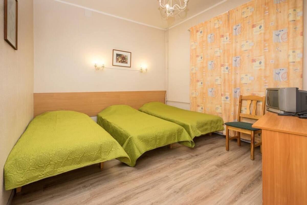 A room with two single beds, a wooden desk, a chair, a television, and a patterned curtain.