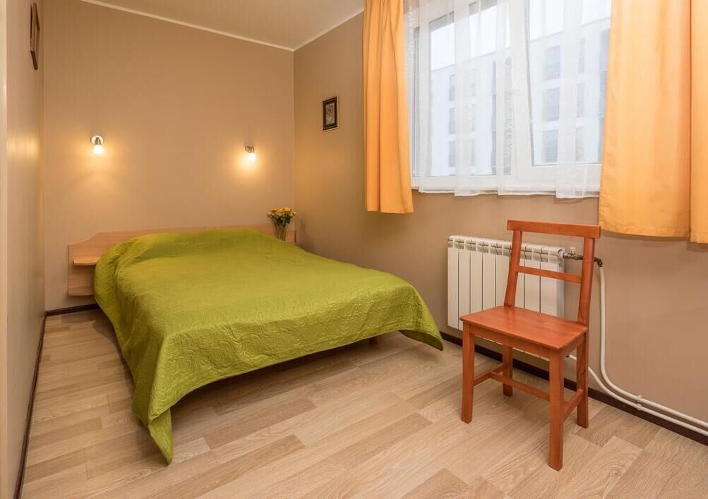 A bedroom with a bed, a chair, a radiator, and a window with curtains.
