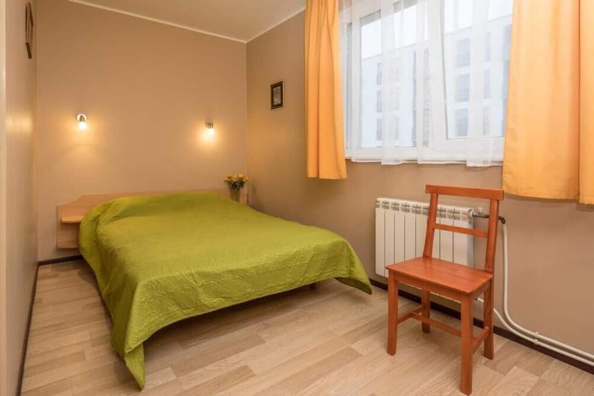 A bedroom with a bed, a chair, a radiator, and a window with curtains.
