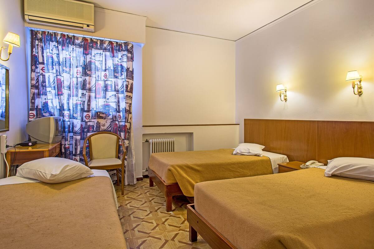 A hotel room with two beds, a desk, a chair, a telephone, and a curtain with a cityscape pattern.