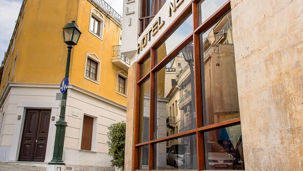 Hotel Nebel numa rua estreita, com um edifício amarelo e outro branco com grandes janelas.