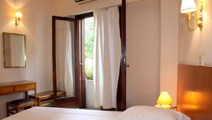 Quarto de hotel com cama, escrivaninha, cadeira, espelho e porta que dá para uma varanda.
