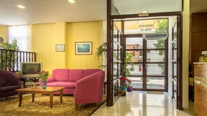 Um saguão de hotel com um sofá vermelho, uma mesa de centro de madeira e uma televisão.