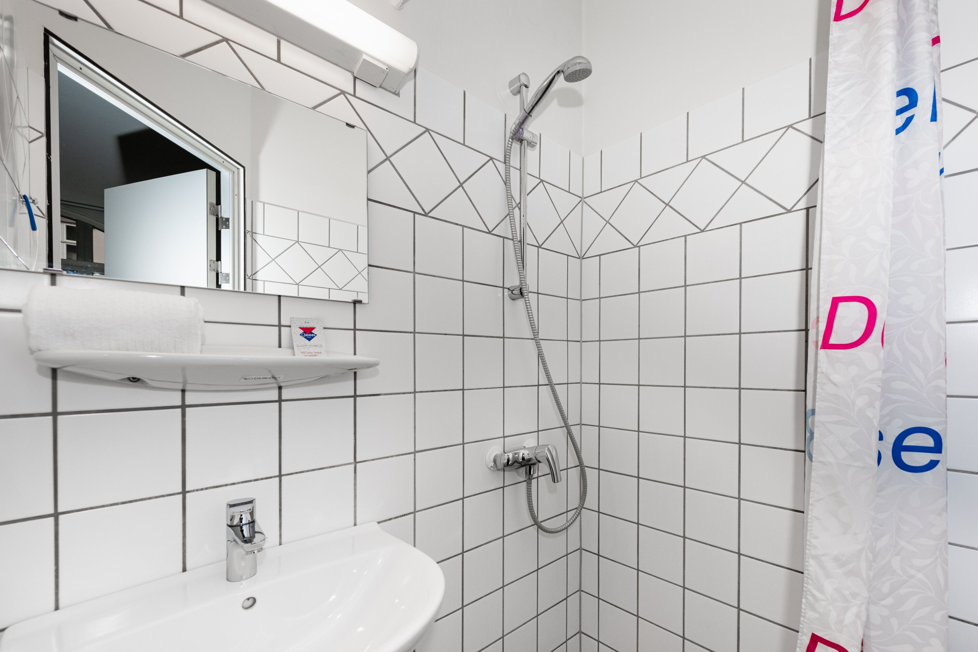 A bathroom with a white sink, mirror, and shower.