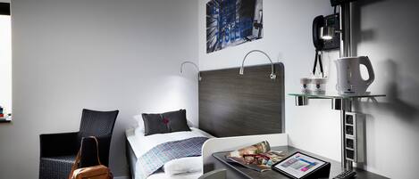 Quarto de hotel moderno com cama, escrivaninha com tablet, máquina de café e televisão na parede.