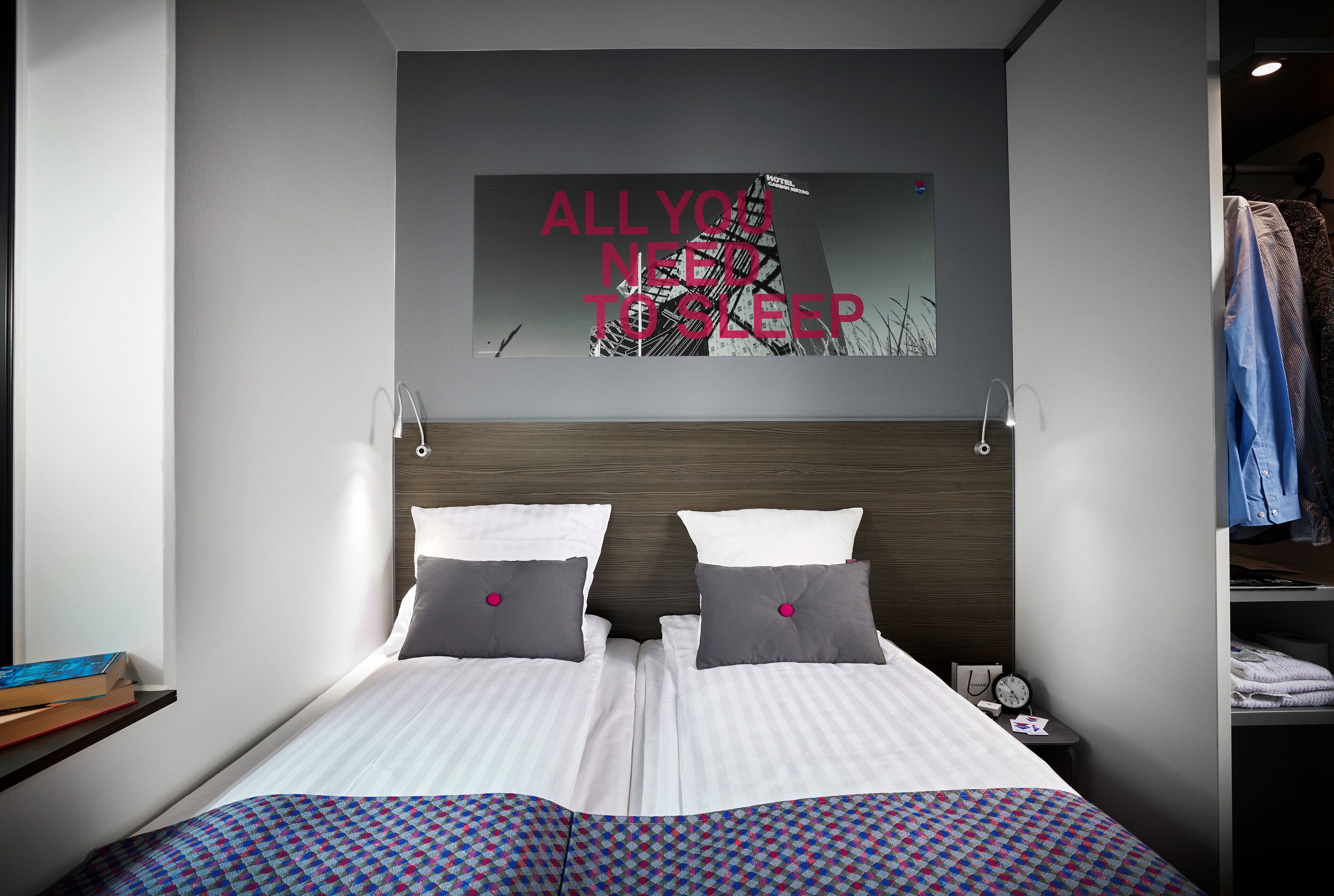 Una habitación de hotel moderna con una cama, una mesita de noche, un reloj y una obra de arte en la pared.