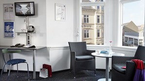A hotel room with a large window, a flat-screen TV, a desk with a telephone, and two wicker chairs. - CABINN Esbjerg Hotel (Esbjerg)
