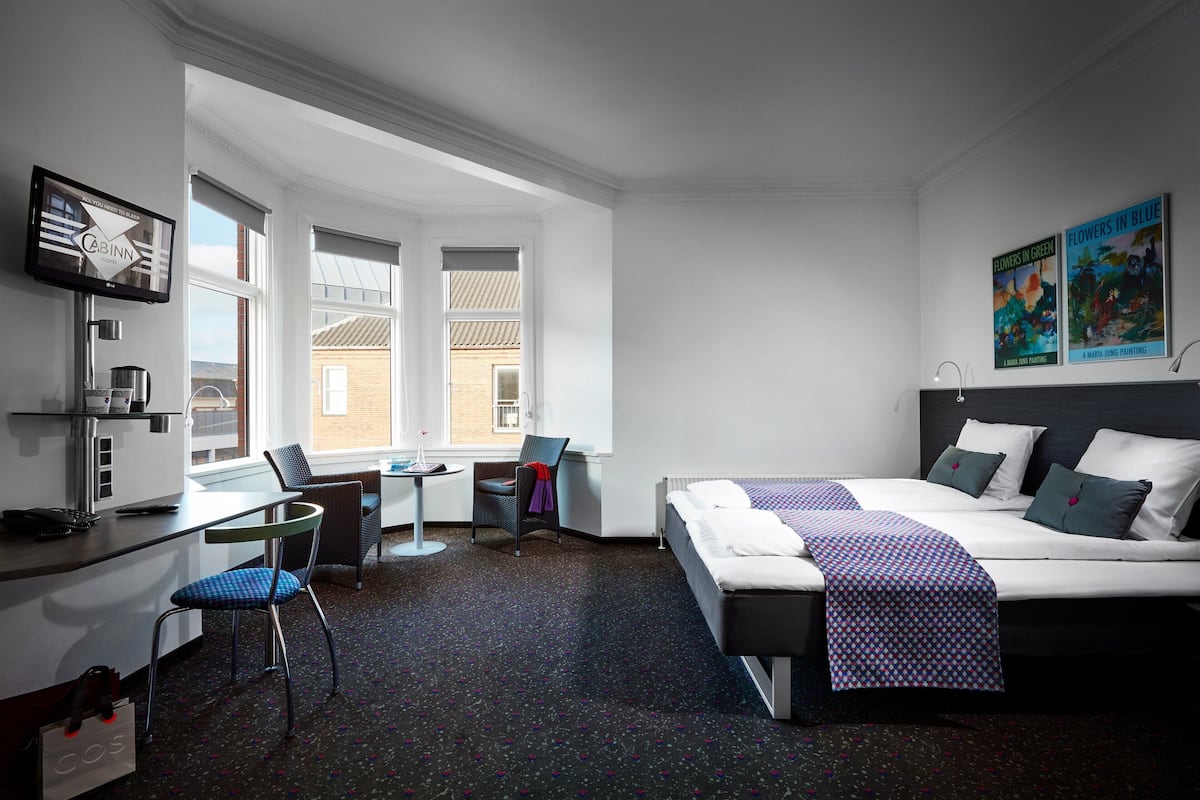 Habitación de hotel con cama, escritorio, silla y una pequeña mesa.
