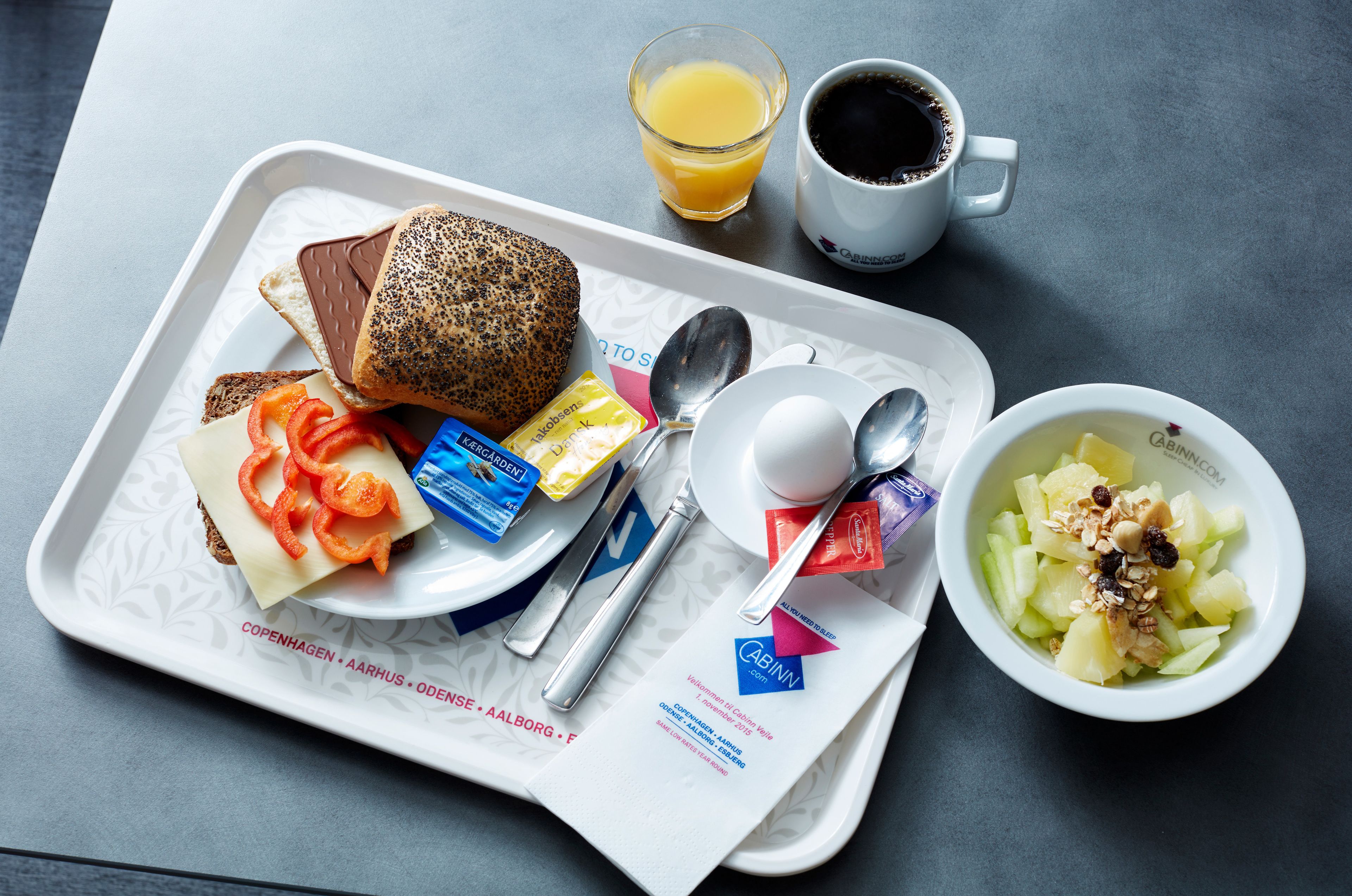 Ein Frühstücksbrett mit Toast, Käse, Marmelade, Butter, einer Schale Obstsalat, einem Glas Orangensaft und einer Tasse Kaffee.