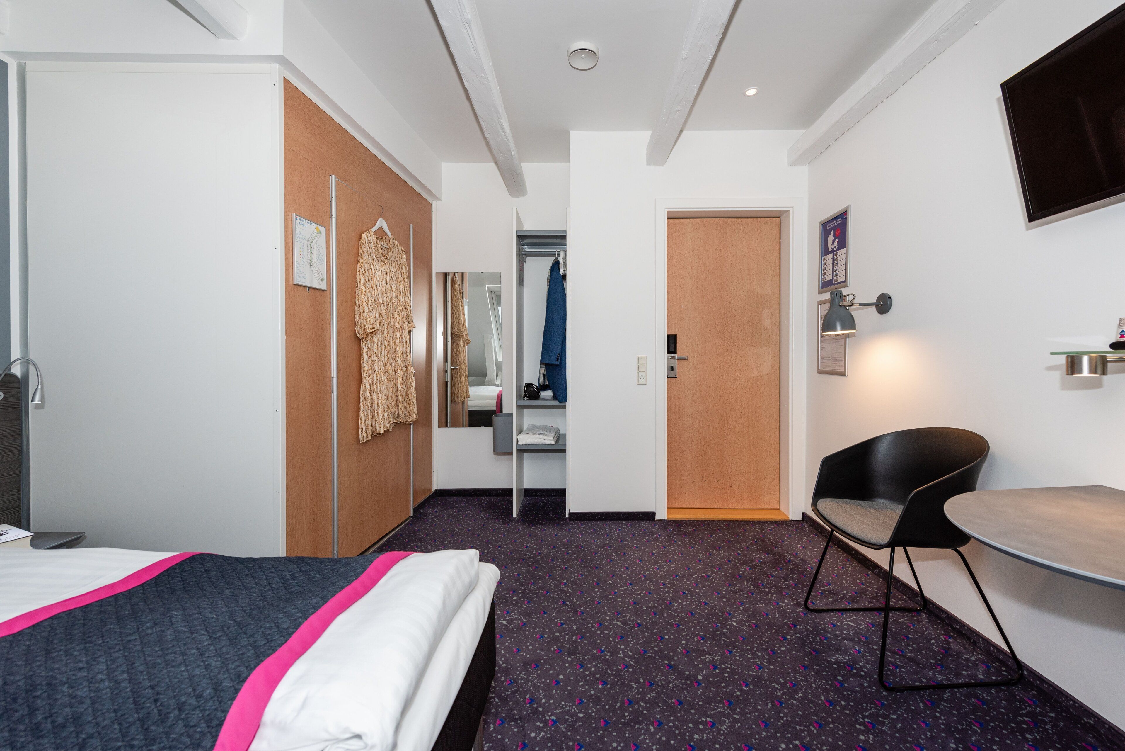 Hotellihuone, jossa on sänky, työpöytä, tuoli, vaatekaappi, peili ja televisio.