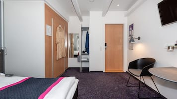 A hotel room with a bed, a desk, a chair, a wardrobe, a mirror, and a television.