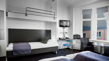 Ein Hotelzimmer mit einem Etagenbett, einem Schreibtisch mit Computer, einem Sessel und einem kleinen Tisch mit Blumenvase.