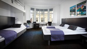 A hotel room with two beds, a desk, and a chair. There are large windows with a view of buildings outside. - CABINN Esbjerg Hotel (Esbjerg)
