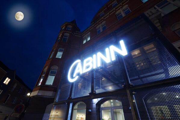 Un edificio con un llamativo letrero iluminado que dice 'CABINN', ventanas amplias y fachada de ladrillo.