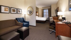 A hotel room with a bed, a desk with a lamp, a blue armchair, a brown sofa, and a small table. - Comfort Suites Troy-I75 (Troy)
