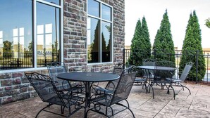 An outdoor patio with stone-tiled flooring, metal tables and chairs, and a brick building with large windows. - Comfort Suites Troy-I75 (Troy)