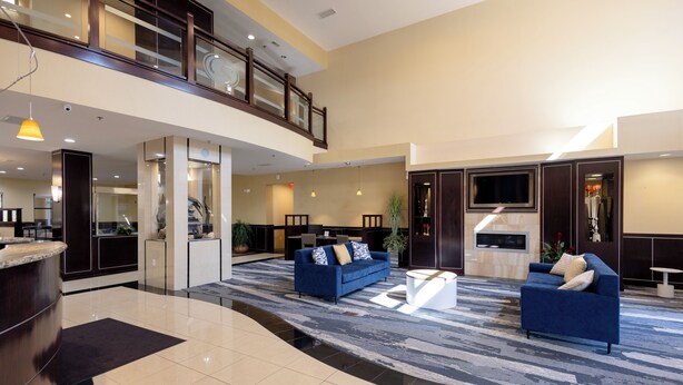 A spacious lobby with a high ceiling, a reception desk, two blue sofas, a coffee table, and a TV mounted on the wall. - Comfort Suites Troy-I75 (Troy)