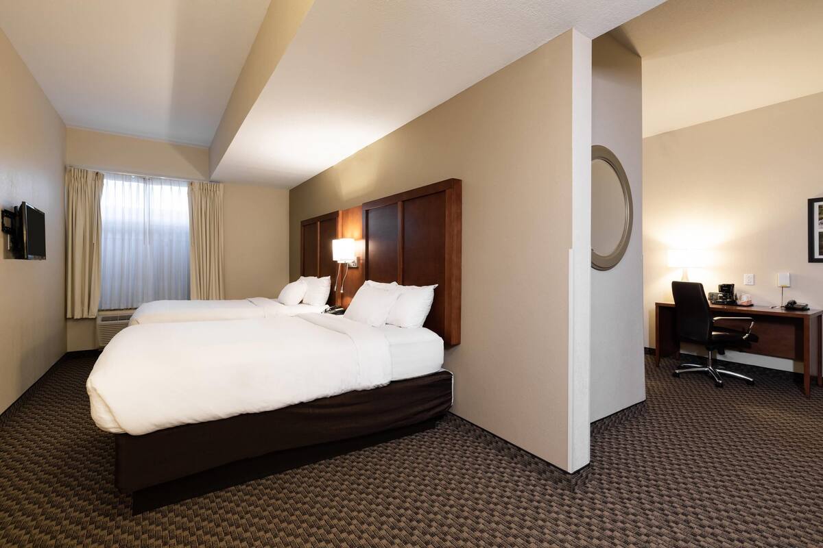 A hotel room with two beds, a desk, a chair, a lamp, and a large mirror.