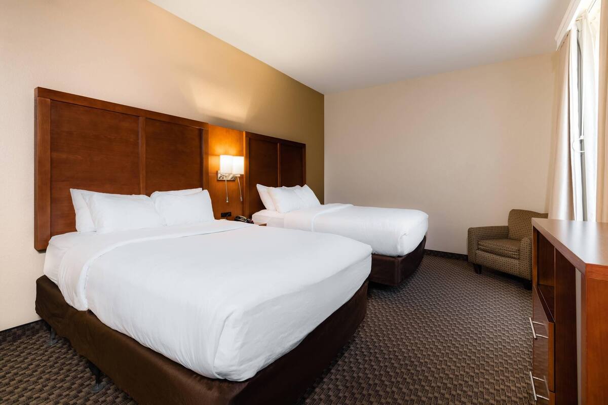 A hotel room with two beds, a desk, a chair, and a lamp.