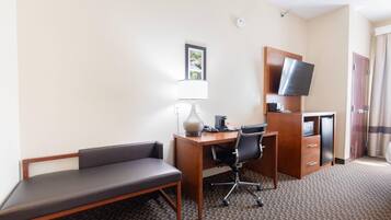 A hotel room with a desk, chair, lamp, television, and a minibar.