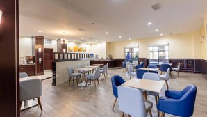 A spacious indoor area with multiple tables and chairs, a counter with a menu, and a large window providing natural light. - Comfort Suites Troy-I75 (Troy)