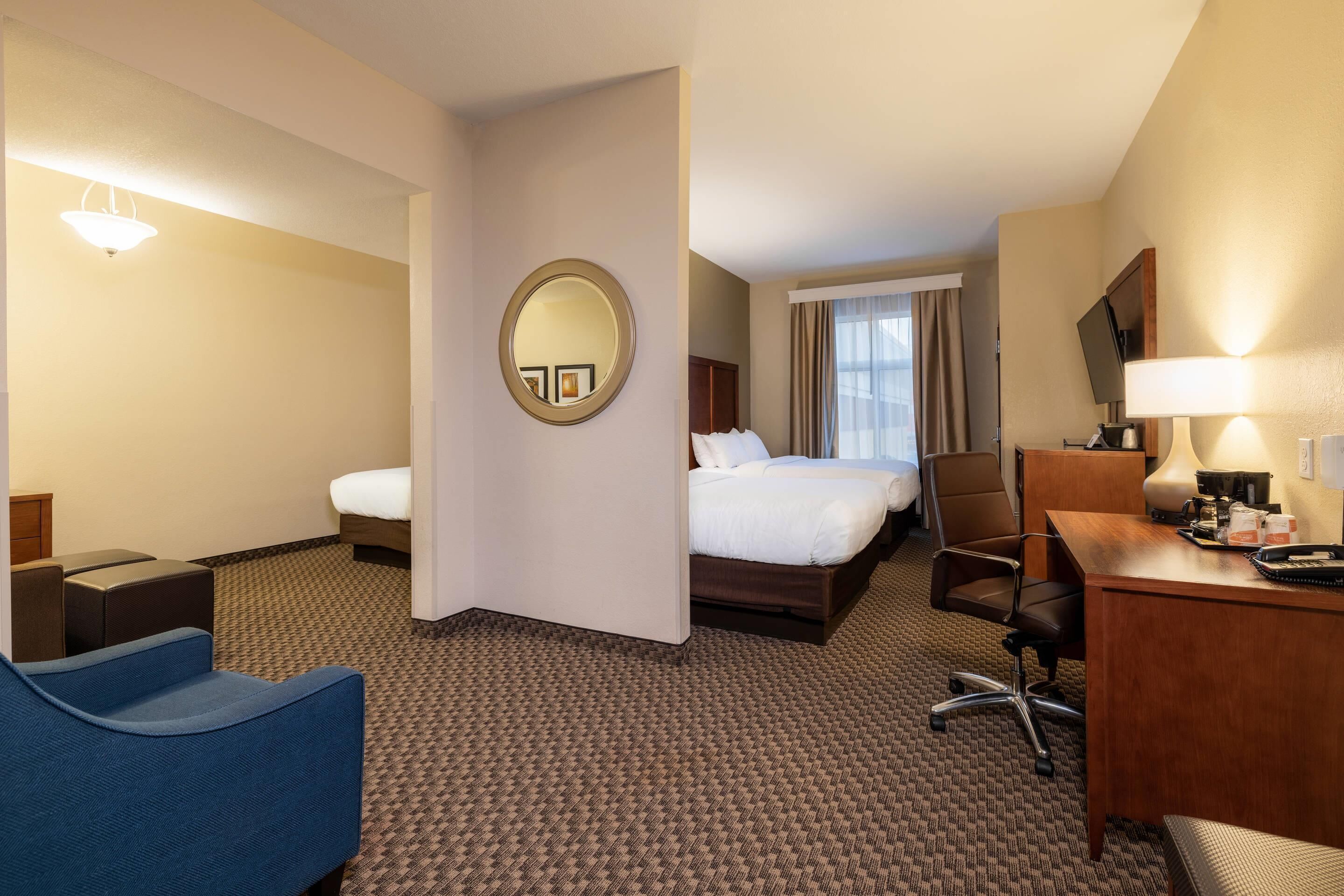Habitación de hotel con cama, escritorio, silla, pequeño sofá, espejo redondo y televisor.