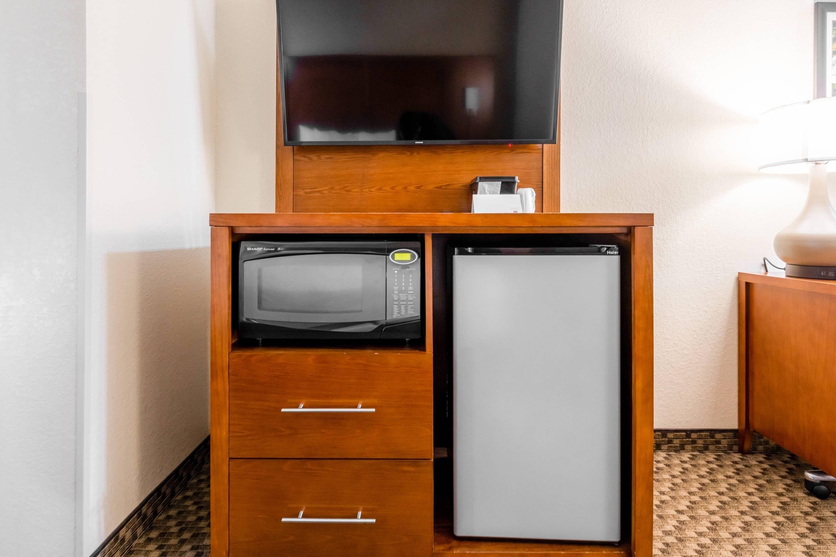 Una kitchenette compacta con microondas, refrigerador y un mueble de madera con cajones.