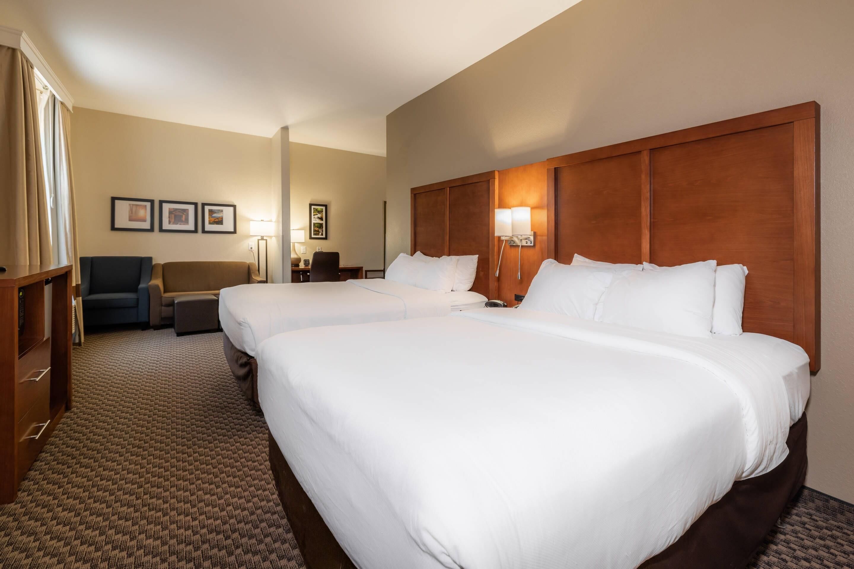 A hotel room with two large beds, a desk, a chair, and a sofa.