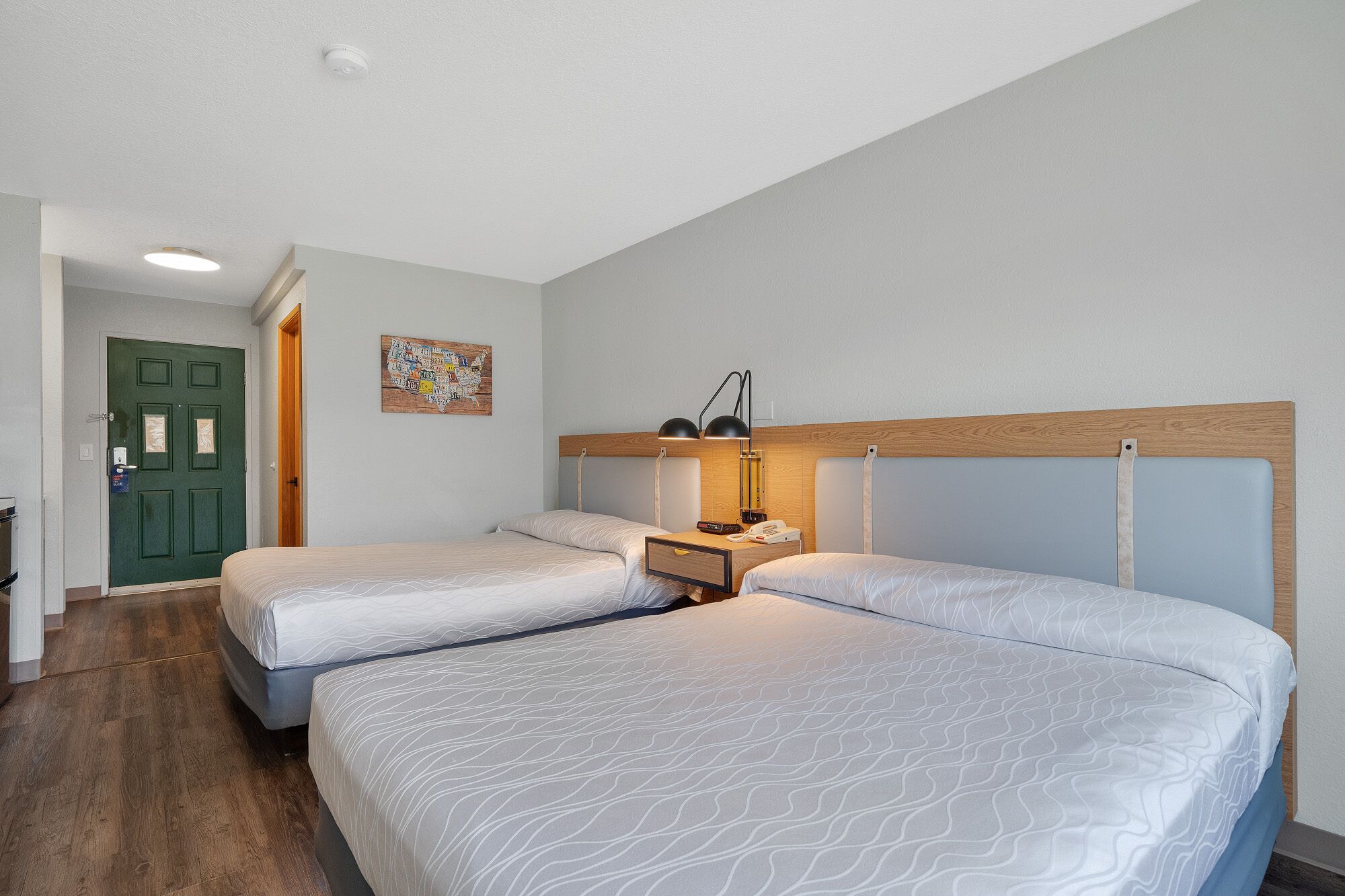 A hotel room with two beds, a wooden headboard, a nightstand with a lamp, and a map on the wall.
