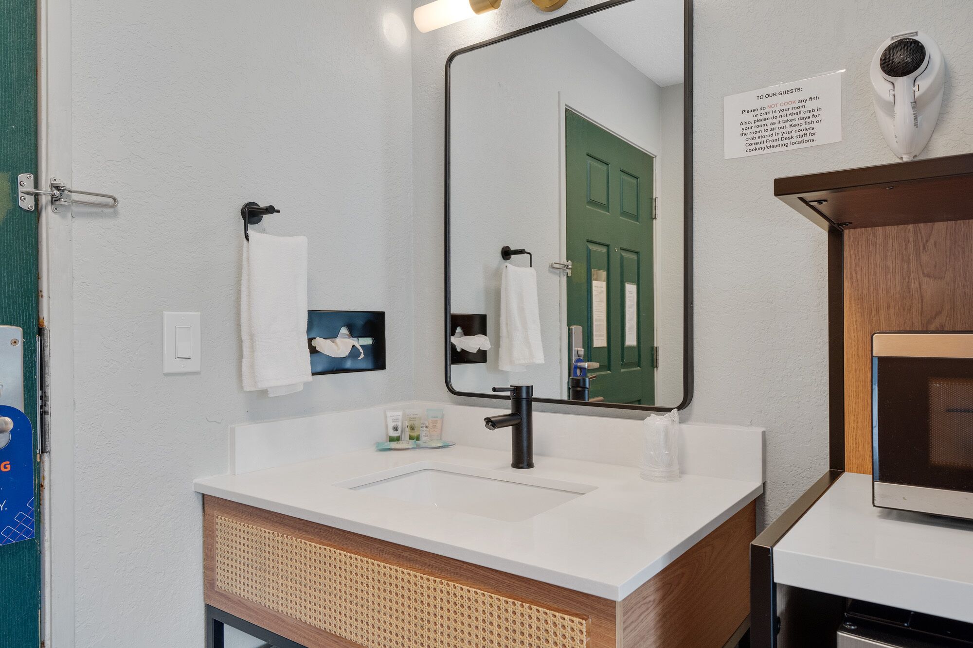 Une salle de bain avec un lavabo blanc, un miroir, une porte verte et un porte-serviettes.