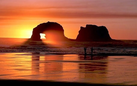 A sunset over a beach with two prominent rock formations silhouetted against the sky.