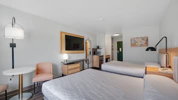 A hotel room with two beds, a desk, a chair, a lamp, a small table, and a wall-mounted TV.