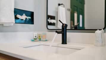 A modern bathroom with a black faucet, a white sink, and a mirror reflecting a towel and a green door.