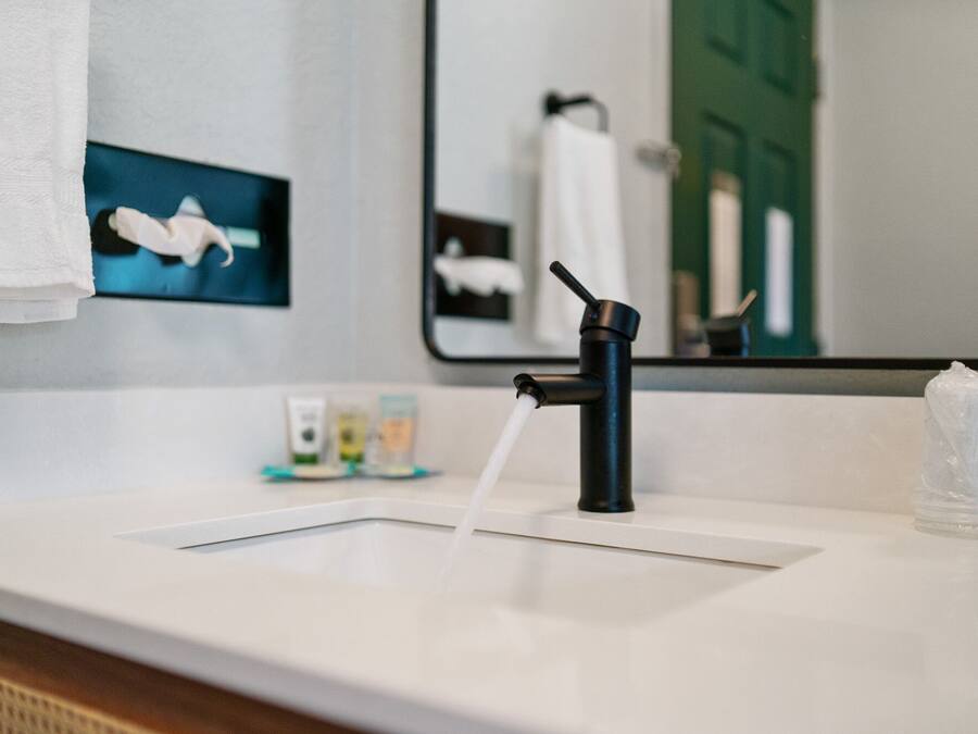 A modern bathroom with a black faucet, a white sink, and a mirror reflecting a towel and a green door.